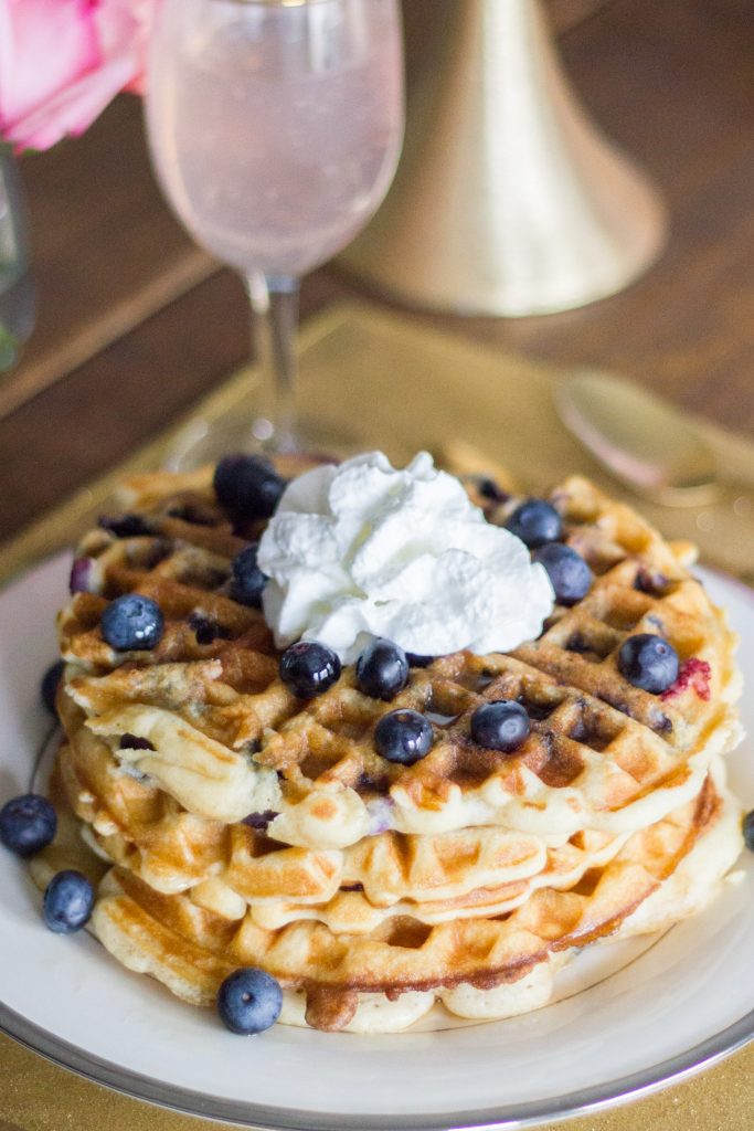 LOVE this idea! "Galentine's Day" was introduced on the show Parks and Recreation. The main character, Leslie Knope, hosts a brunch for her gal pals every year the day before Valentine's Day. Waffles are her favorite food, so this Galentine's Day brunch featuring blueberry waffles is perfect!