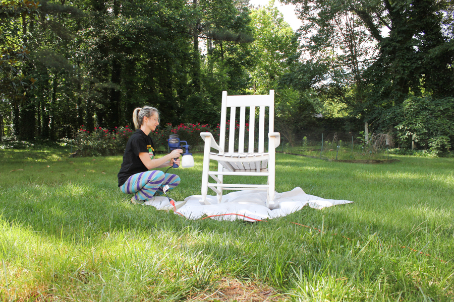 Blogger using a paint sprayer to paint a rocking chair.