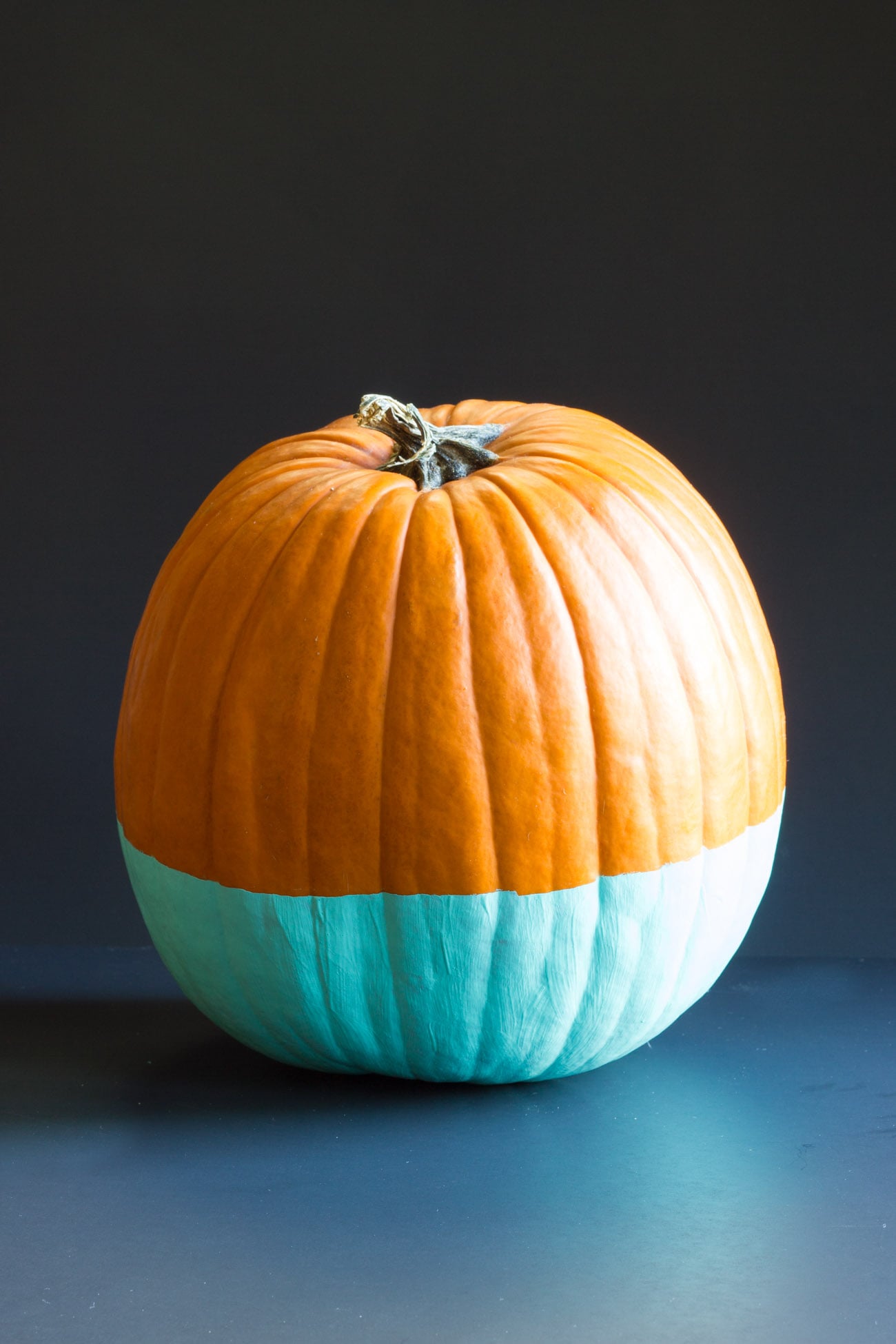 Orange pumpkin with a crisp aqua-painted lower section on a dark blue background