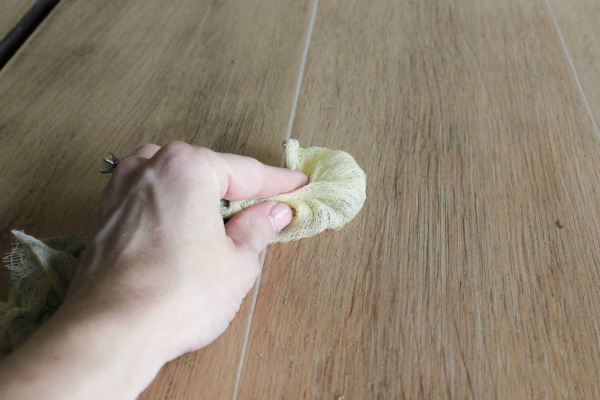 Removing dust from sanded furniture with a tack cloth.